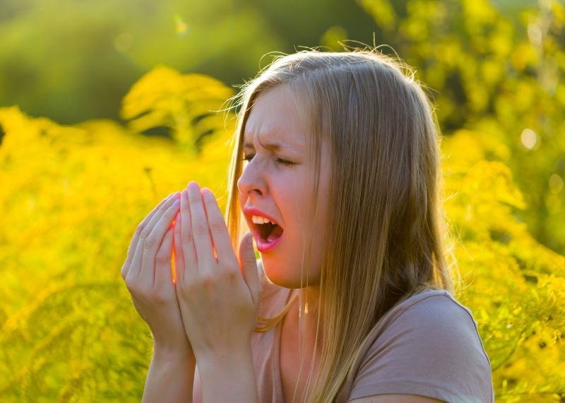woman sneezing into hands 